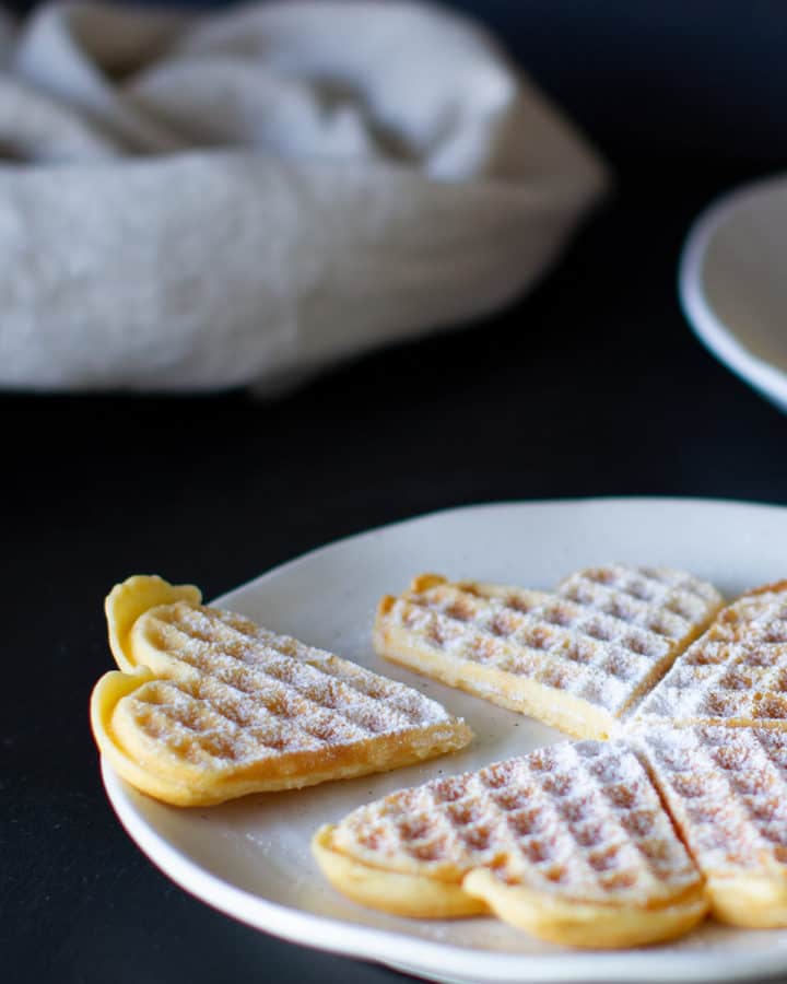 Heart shaped German waffles dusted with icing sugar on a white plate