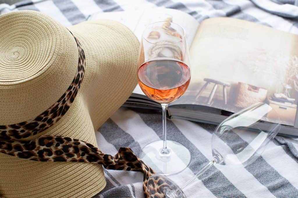 A glass of Rosé with beach gear including a sunhat, book and towel