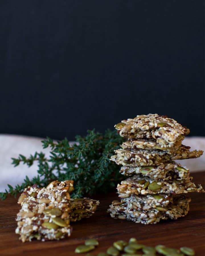 A stack of five seed crackers on a wooden board, moody scene.