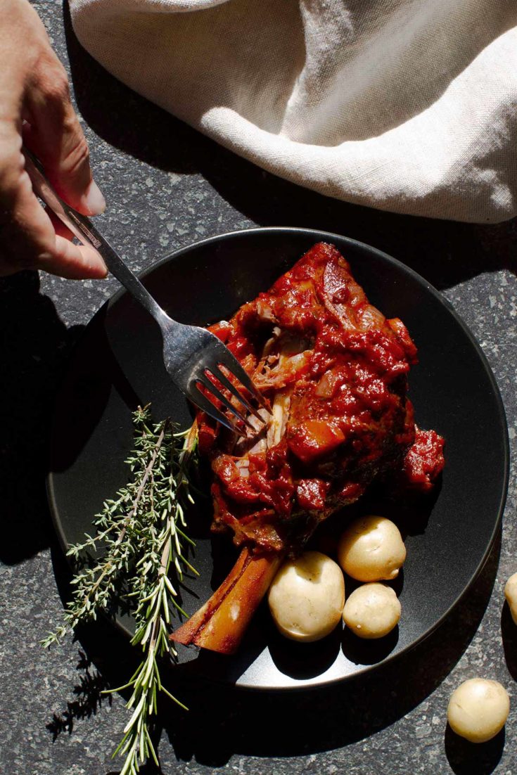 Moroccan Lamb Shanks with potatoes and fresh herbs on a black plate