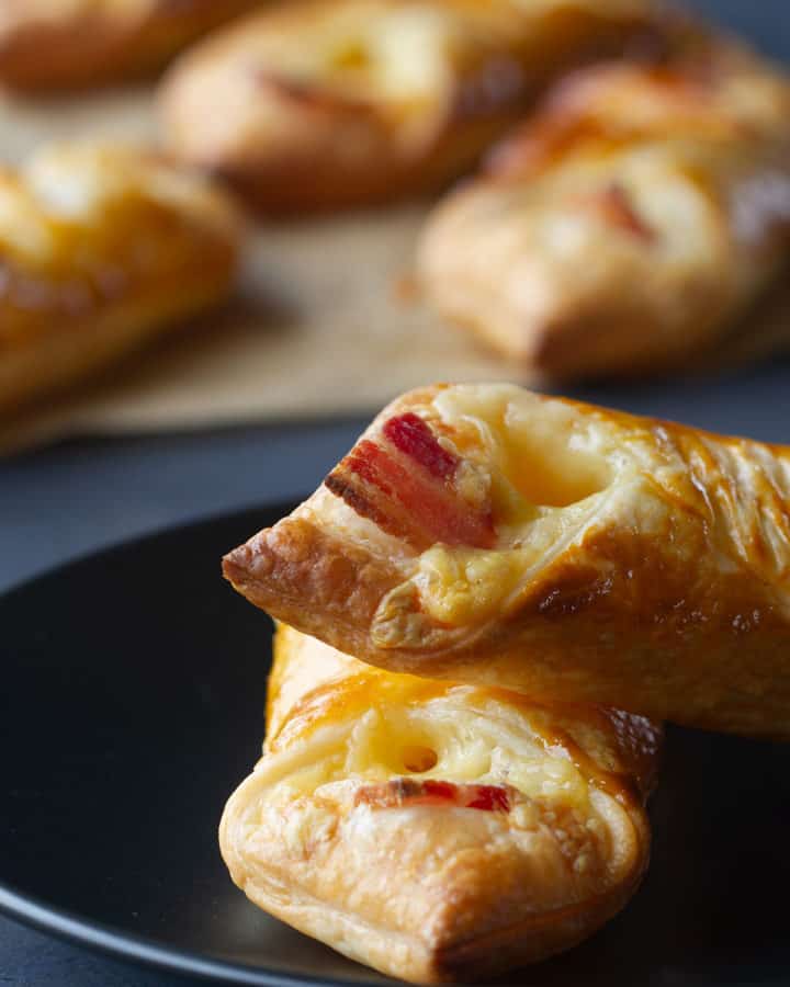 Two zoomed in cheese and bacon turnovers on a black plate