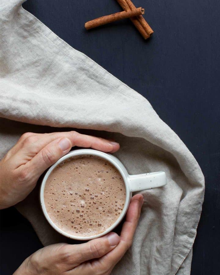 A moody flatlay scene of hands holding a cup of hot chocolate following the hot cacao recipe