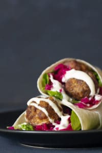 Two meatball wraps on a black plate.