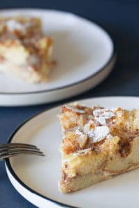 A slice of sourdough bread pudding on a white plate. Another plate is blurred out in the background.