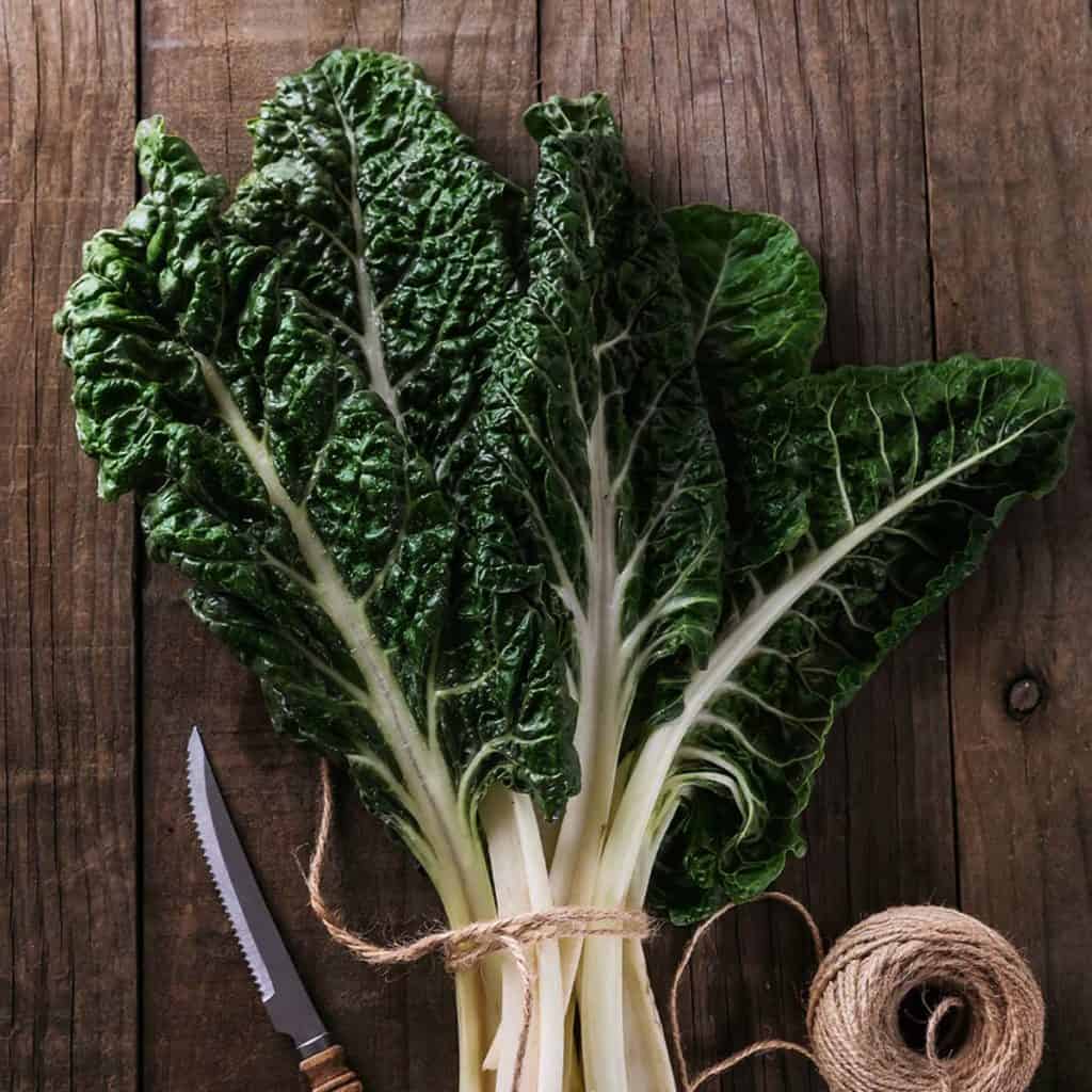 A bunch of silverbeet on a wooden board next to a knife and twine.